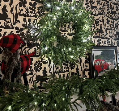 A Christmas wreath with white lights on a textured wall beside art pieces.